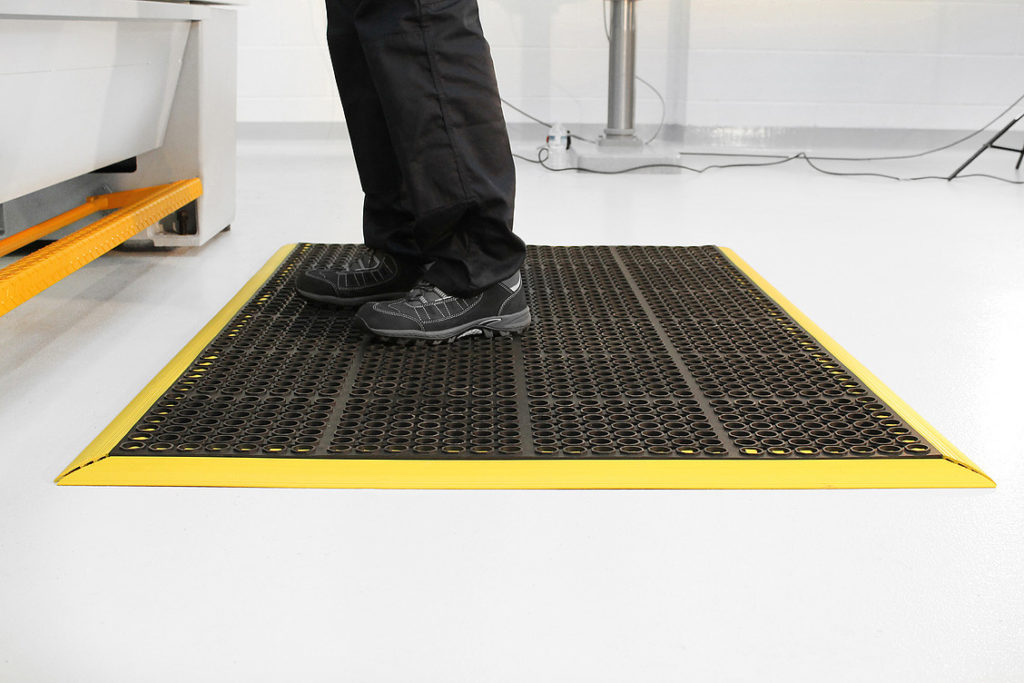 Man standing on a black and yellow deluxe workplace anti-fatigue mat