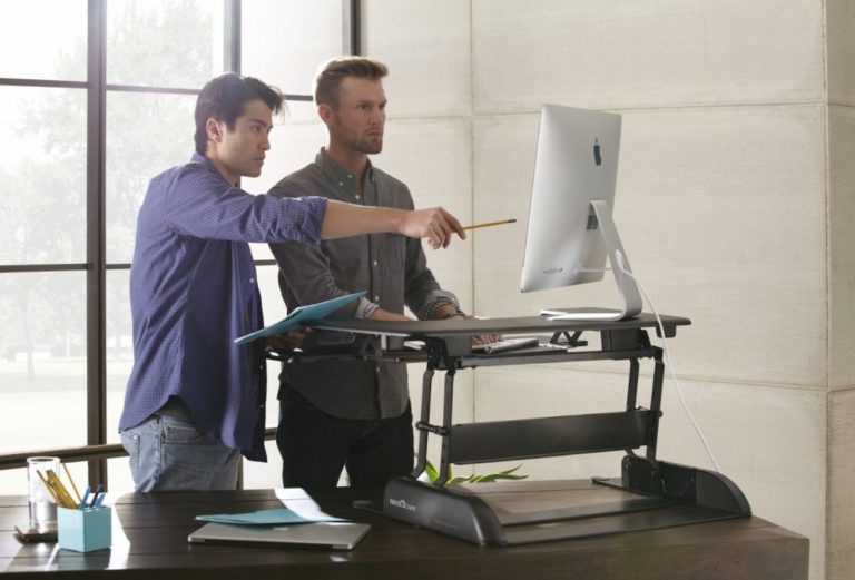 men looking at a laptop behind a standing desk