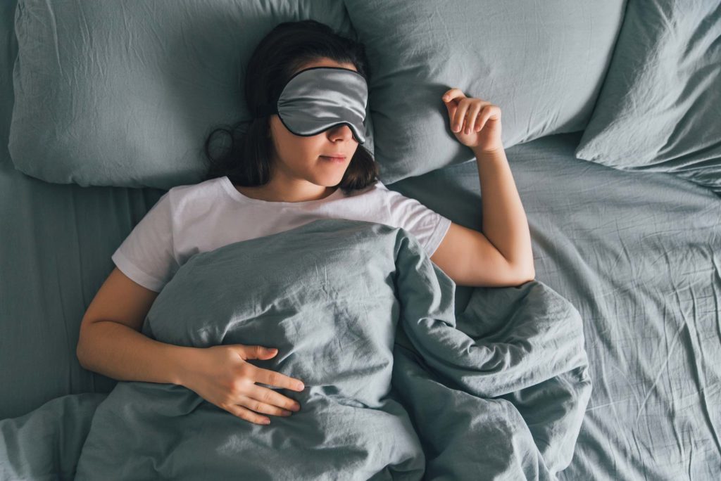 Woman asleep with an eye mask in a grey bed